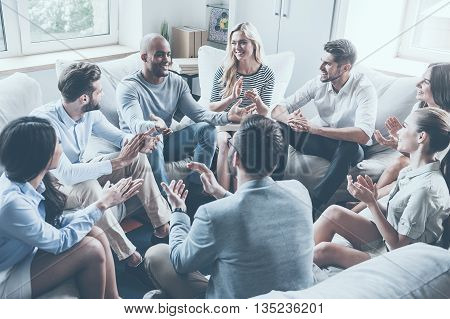 Applauding their achievements. Group of young cheerful people sitting in circle and applauding while one man gesturing and smiling