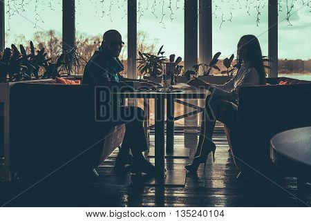 The silhouette of the love couple sitting at table in a cafe