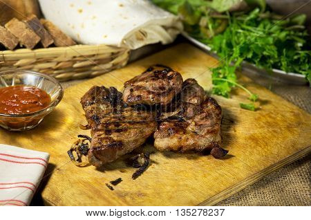 Grilled meat with onion ketchup herbs and bread on a wooden oard