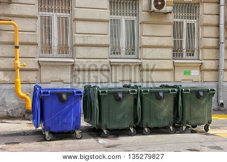 four blue and green color plastic dumpsters on the city street near building in Moscow