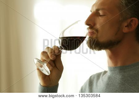 Handsome middle-aged man tasting red wine, close-up
