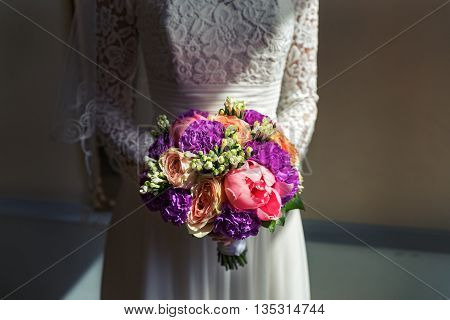 Bouquet of peonies in the hands of bride. Shot with contrasting light.