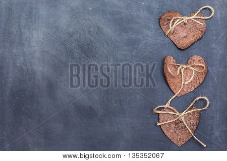 Three (3) decorative hearts made from tree bark on chalkboard, positioned on right side of the photo. Hearts decorated with eco twine. Eco decor. St. Valentines greeting card idea. Handmade design.