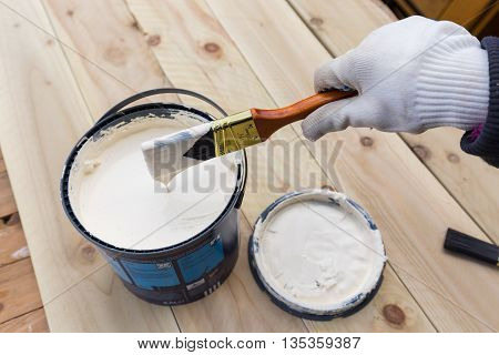 Holding painting brush in the jar with the white paint. Painting timber boards outside with the white paint or white coloured emulsion using 2 inches painting brush.