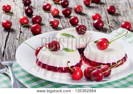 Italian dessert of cherry juice and sweetened cream thickened with gelatin and molded on a white dish on a table napkin with dessert forks and cherries on a dark wooden background close-up