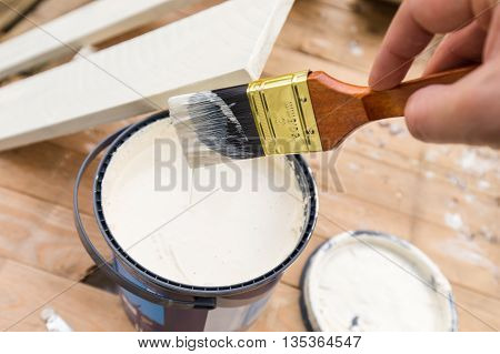 Holding painting brush over the jar with the white paint. Painting timber boards outside with the white paint or white coloured emulsion using 2 inches painting brush.