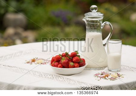 Bowl of strawberries standing on the table with glass of milk. Jug full of milk beside bowl of strawberries. Summer breakfast. Summer desert. Picnic idea. Healthy option