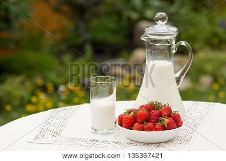 Bowl of strawberries standing on the table with glass of milk. Jug full of milk beside bowl of strawberries. Summer breakfast. Summer desert. Picnic idea. Healthy option