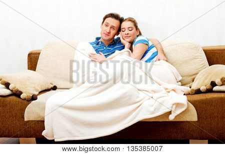 Smiling loving couple sitting on couch with blanket