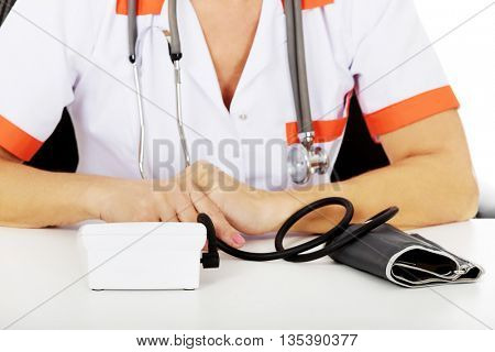 Elderly female doctor or nurse sitting behind the desk with bloog preasure gauge