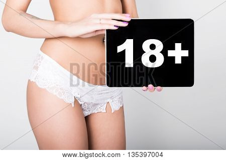 technology, internet and networking - close-up ass of girl in lacy lingerie, holding a tablet pc with eighteen plus sign. Adult content.