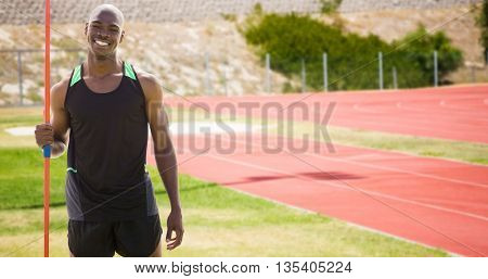 Front view of happy sportsman is holding a javelin against athletic field on a sunny day