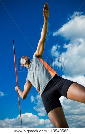 Low angle view of athletic man preparing his javelin throw against low angle view of blue sky