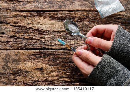 Drug Addict Holding Spoon With Drug In Hand And A Syringe On A Wooden Background