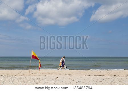 Tisvilde, Denmark - June 20, 2016: People walking behind red and yellow swimming area flag at Tisvilde beach.