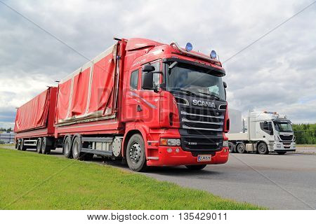 FORSSA FINLAND - JUNE 21 2016: Red Scania R560 with side dumping trailer parked at a truck stop with green grass grey sky and white Iveco truck on the background.