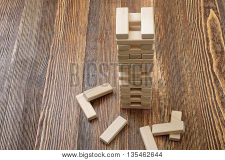 The tower of wooden blocks placed on a table.. Removing blocks from a tower. Keeping balance. Full concentration. Entertainment activity. Game of physical and mental skill. Close-up photo.