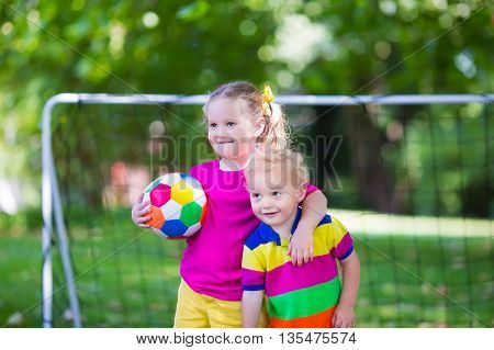 Two happy children playing European football outdoors in school yard. Kids play soccer. Active sport for preschool child. Ball game for young kid team. Boy and girl score a goal in football match.