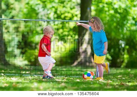 Two happy children playing European football outdoors in school yard. Kids play soccer. Active sport for preschool child. Ball game for young kid team. Boy and girl score a goal in football match.