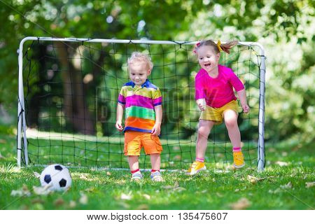Two happy children playing European football outdoors in school yard. Kids play soccer. Active sport for preschool child. Ball game for young kid team. Boy and girl score a goal in football match.