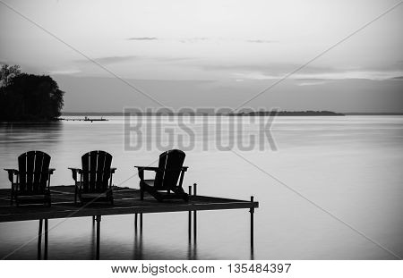 Three cottage chairs in a row on a dock at the cottage at dusk