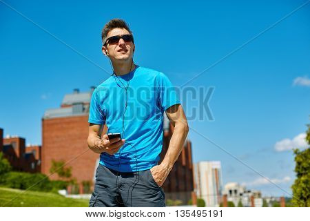man runner athlete warming up and stretched before jogging along a city bay at the early morning. man training outdoors in park with phone in hand and headphones. man fitness sunset jogging workout wellness concept.