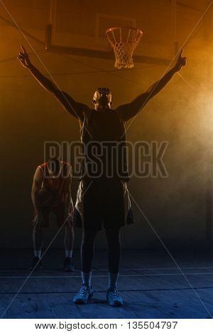 Victorious basketball player raising his arms up while his rival looking down