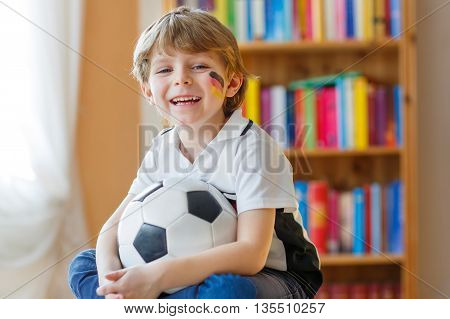 Little blond preschool kid boy with ball watching soccer european cup game on tv. Funny child fan having fun and cheering winning football team. Champions league concept.