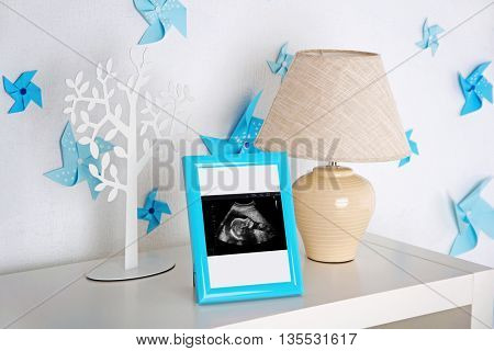 Lamp and photo frame with ultrasound scan of baby on shelf in children room