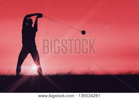Front view of sportsman practicing hammer throw against red sky over grass