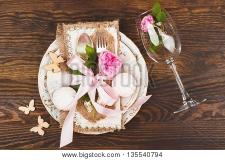 Table serving: tableware and silverware with decorations. Light pink roses marshmallows and wooden butterflies on the wooden background