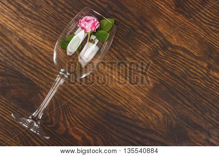 Empty wineglass with small light pink rose inside on the wooden background with blank copy space area for text or slogan