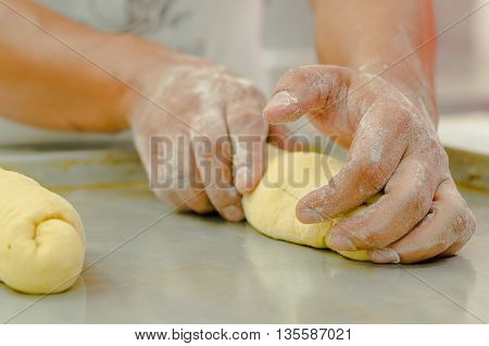 Hands of baker working, kneading and rolling bread dough, shaping into loaf before cooking.