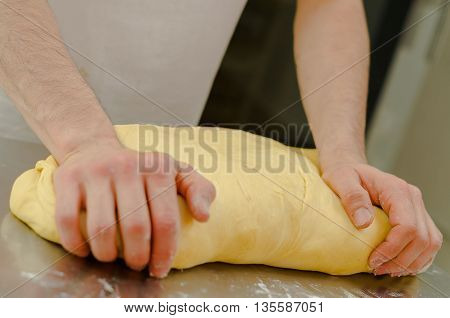 Hands of baker working, kneading and rolling bread dough, shaping into loaf before cooking.