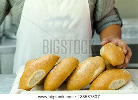 Pile of fresh bread loafs, baker standing behind with only apren and arms visible, bakery concept.