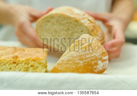 Bakers hands placing half cut loaf of bread onto white plate next to other breads.