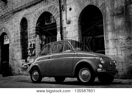 Gubbio, Italy - May 13, 2011; Gritty monochrome image traditional back Italian street with iconic small car surrounded by old stone buildings vignette