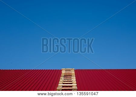 ladder on the gable roof. wooden ladder lying on the rooftop. clear blue sky. fix the roof before it starts to rain. go through the roof. copy space for your text