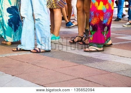 Group of casual men and women standing on paving in a low angle view of their feet in sandals jeans shorts and caftans or long summer skirts with foreground copy space