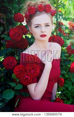 Lady vamp in crimson red dress with naked shoulders and red roses in her hair