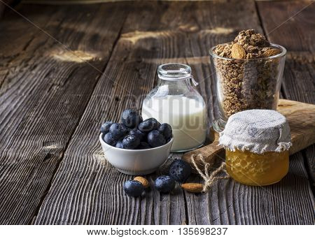 Healthy breakfast ingredients. Cereal, chocolate muesli, fresh blueberries, jar with honeycombs, rustic milk bottle on a simple plank dark background in rustic style. selective focus