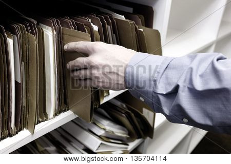 Businessman reaching for files on shelf for information storage