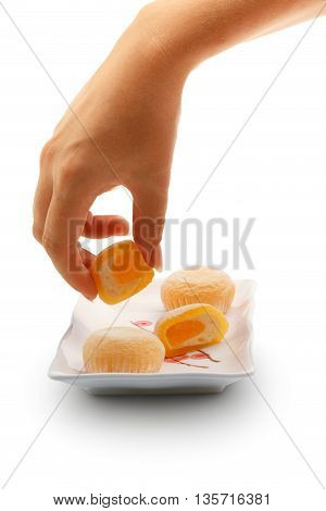 Beautiful elegant female hand taking mango mochi dessert from white square ceramic plate with japanese rice cakes isolated on white background.