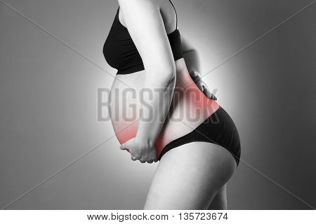 Caucasian pregnant woman in black lingerie with back and abdominal pain on gray studio background. Pregnancy concept