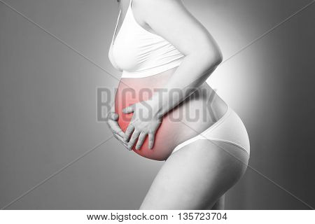 Caucasian pregnant woman in white lingerie with abdominal pain on gray studio background. Pregnancy concept