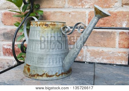 A old rusting watering can on a shelf.