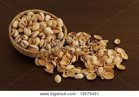 Pistazien In verwobenen Schüssel mit verschüttete Nutshells auf dunklen Holztisch