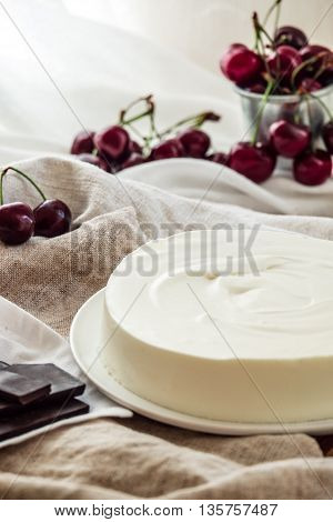 Vanilla bavarian mousse cake with cherries and dark chocolate. Made with cream cheese and whipped cream. White plate and light background.