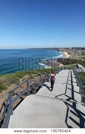 A woman walks along the a newly constructed section of the Newcastle coastal walk on a beautiful sunny day. Bar Beach and Merewether beaches are seen in the distance.