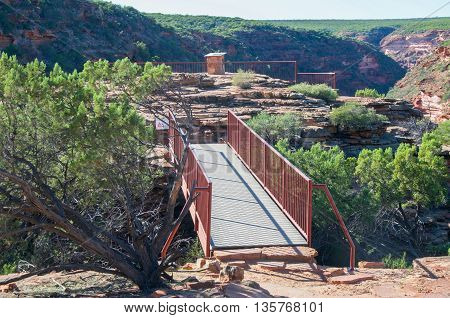 Pedestrian bridge at the Z-bend lookout in Kalbarri National Park with red sandstone and native green flora under a clear blue sky in Kalbarri, Western Australia.